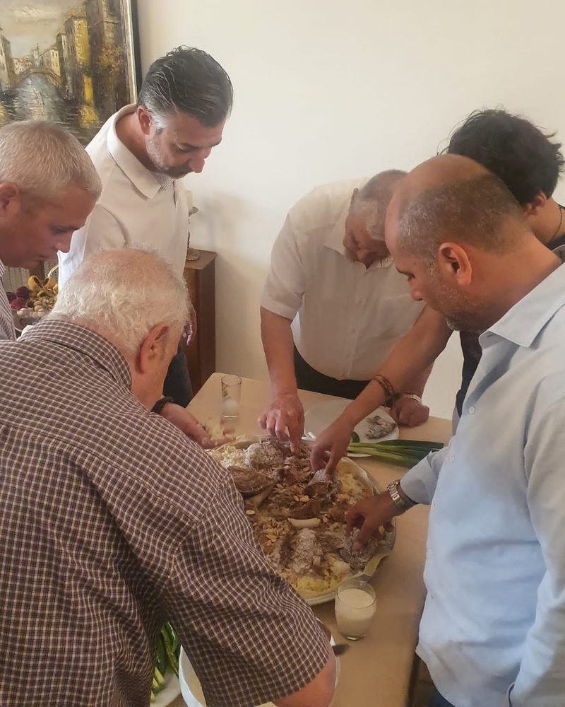 Men of a family sharing mansaf by hand around one tray