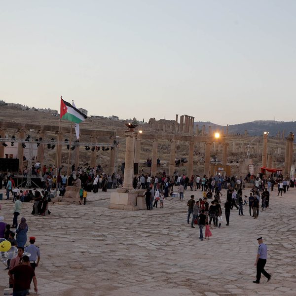 The Oval Plaza of Jerash at dusk, with a Jordanian flag above the crowd