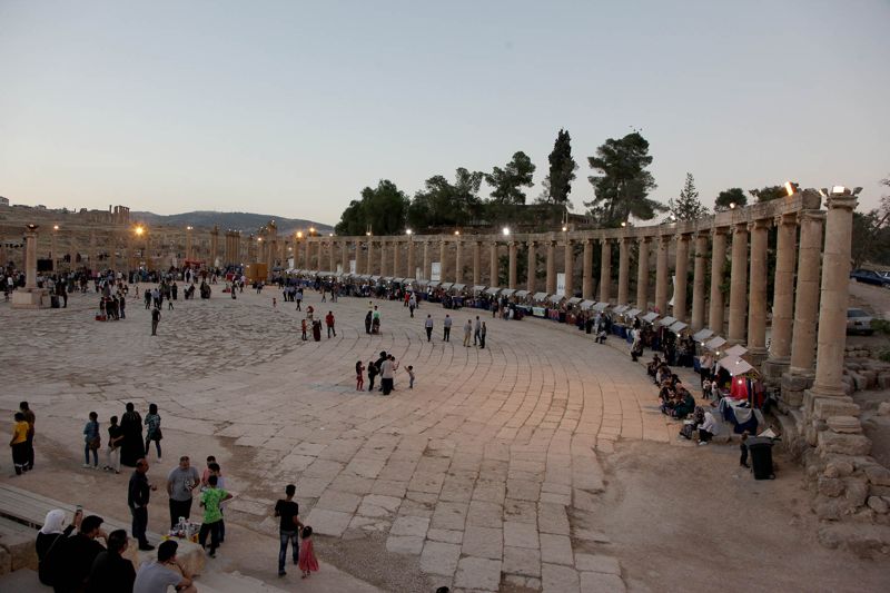 Families and friends walking across the colonnaded Oval Plaza in Jerash at dusk