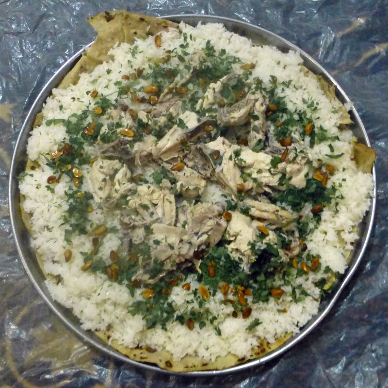 A tray of mansaf seen from above: rice, lamb, pine nuts and parsley over thin bread