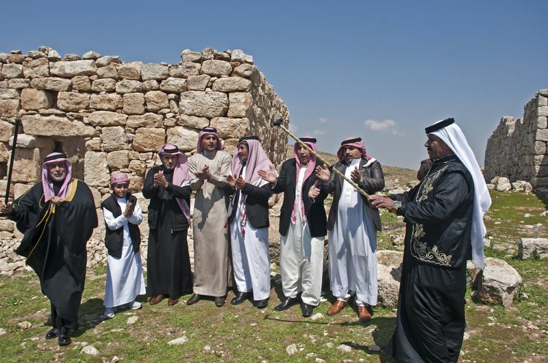 Men in traditional Jordanian dress gathered among old stone ruins