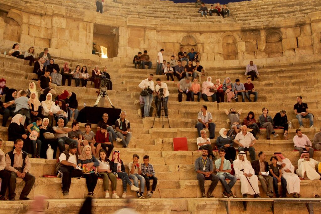 An audience seated on the steps of a stone theatre